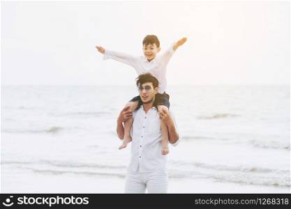 Happy father carrying his son on the neck on a tropical sand beach in summer.