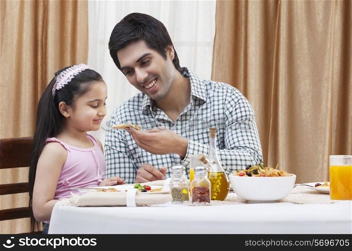 Happy father feeding his cute daughter a piece of pizza at restaurant