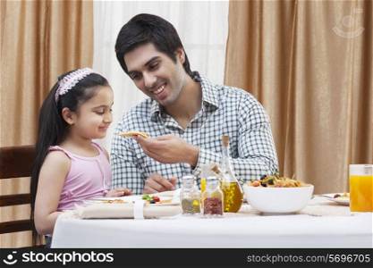 Happy father feeding his cute daughter a piece of pizza at restaurant