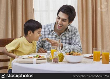 Happy father feeding piece of pizza to his son at restaurant