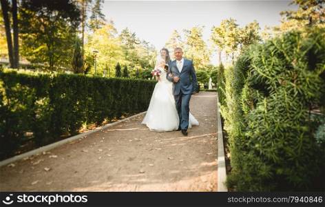 Happy father leads beautiful bride to the altar at park
