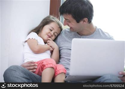 Happy father looking at cute daughter sleeping while using laptop at home