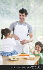 Happy father preparing food with little daughters at home