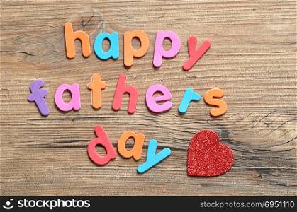Happy fathers day on a wooden background with a red heart