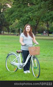 Happy fatty asian woman posing with bicycle outdoor in a park