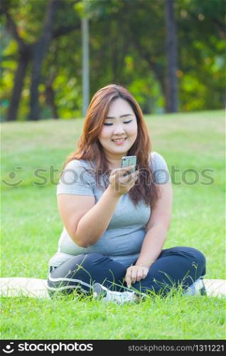 Happy fatty asian woman using mobile phone outdoor in a park