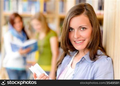 Happy female brunette student at library with books high school