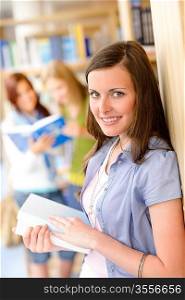 Happy female brunette student at library with books high school