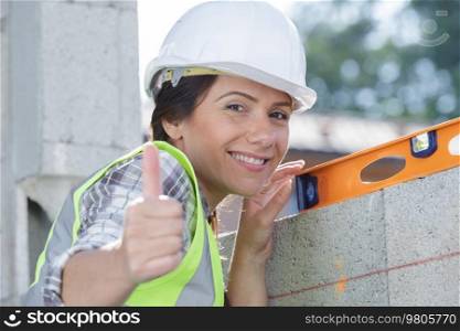 happy female builder with a level shows thumb-up