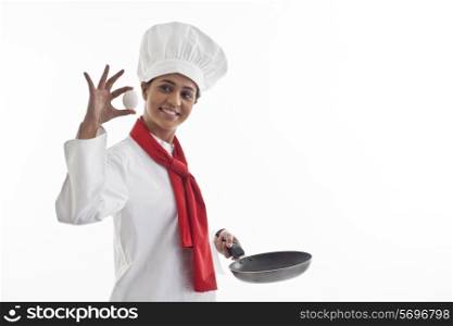 Happy female chef holding an egg and frying pan isolated over white background