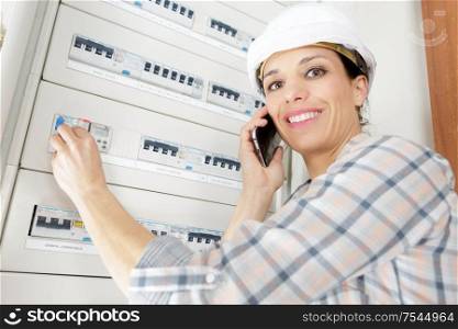 happy female electrician on the phone with fuseboard