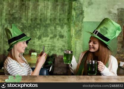 happy female friends celebrating st patrick s day together with drinks smartphone