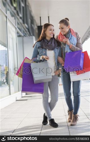 Happy female friends communicating while carrying shopping bags on sidewalk