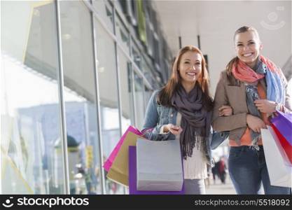 Happy female friends with shopping bags walking by store