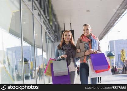 Happy female friends with shopping bags walking on sidewalk