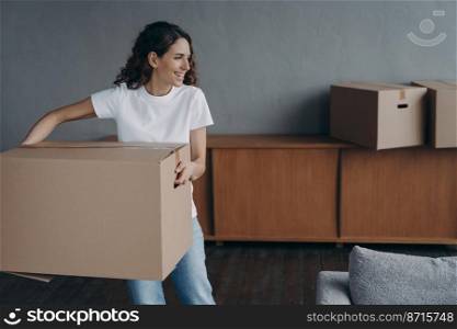 Happy female homeowner carrying cardboard box to living room relocating to new home. Hispanic woman packing things on moving day. Mortgage, real estate tenancy, parcel delivery service advertising.. Female carrying cardboard box to room on moving day. Mortgage, tenancy, parcel delivery service ad