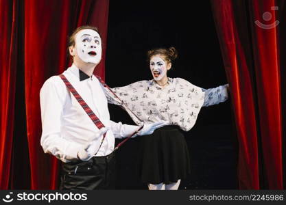 happy female mime looking male mime holding suspender stage
