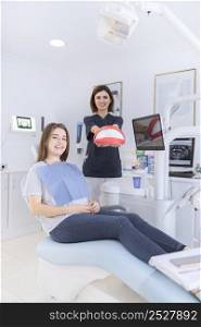 happy female sitting dental chair front dentist holding teeth model