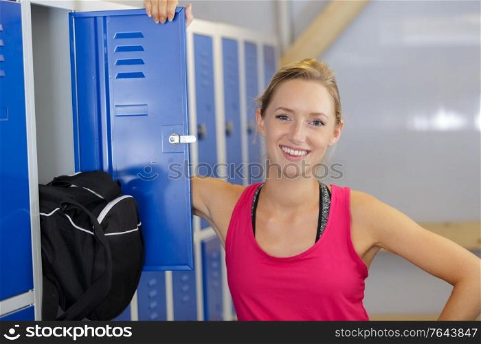 happy female sportswoman next to locker