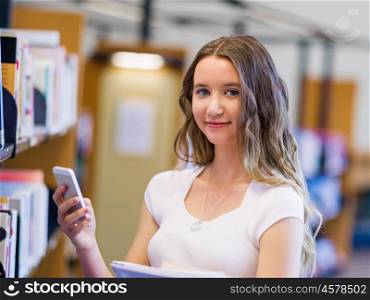 Happy female student holding books at the library. Happy young female student holding books and her mobile phone at the library