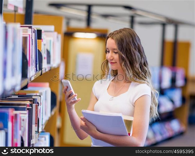 Happy female student holding books at the library. Happy young female student holding books and her mobile phone at the library