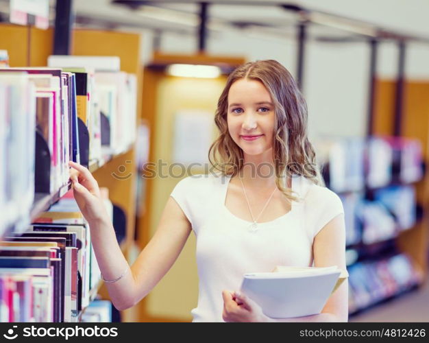 Happy female student holding books at the library. Happy young female student holding books at the library