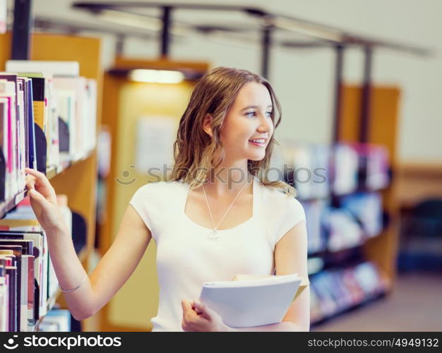 Happy female student holding books at the library. Happy young female student holding books at the library