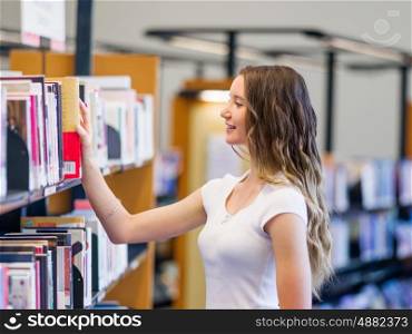 Happy female student picking up books at the library. Happy young female student choosing books at the library