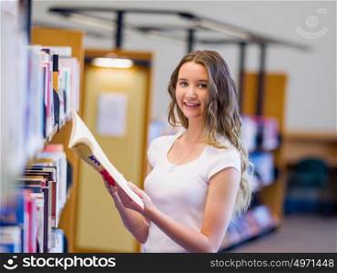 Happy female student picking up books at the library. Happy young female student choosing books at the library