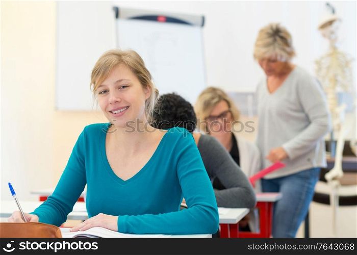 happy female student reading her textbook sitting in classroom
