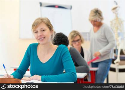 happy female student reading her textbook sitting in classroom