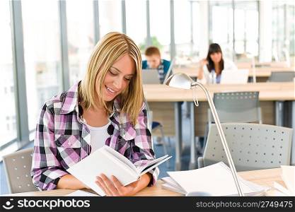 Happy female student with book in classroom, schoolmates in background
