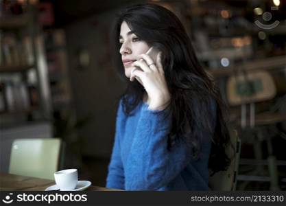 Happy female talking on mobile phone sitting in cafe seen through glass window