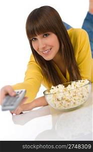 Happy female teenager watching television holding remote control, eating popcorn