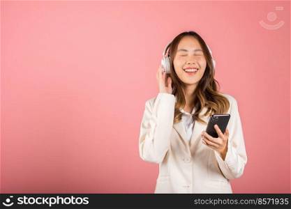 Happy female using mobile phone listens loud song, Portrait of Asian beautiful young woman has fun close eyes listening music with headphones in smartphone app, studio shot isolated on pink background