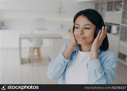 Happy female wearing wireless headphones listening to music, podcast or audio book, enjoying perfect sound quality. Smiling calm woman listen to positive affirmations in headset, relaxing at home.. Happy female in headphones listen to music, podcast or audio book enjoying perfect sound at home