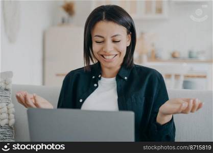 Happy female working on laptop, surprised by incredible good news, reading email at home. Delighted woman looks at computer screen spreading hands in amazement after unexpected win in online lottery.. Happy young female working on laptop, surprised by incredible good news, reading email at home