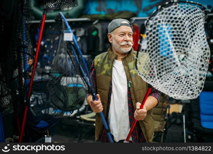 Happy fisherman choosing net in fishing shop, hooks and baubles on background. Equipment and tools for fish catching and hunting, accessory choice on showcase in store, bait assortment. Happy fisherman choosing net in fishing shop