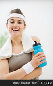 Happy fitness woman with towel on shoulders holding bottle of water