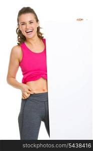 Happy fitness young woman checking body fat and showing blank billboard