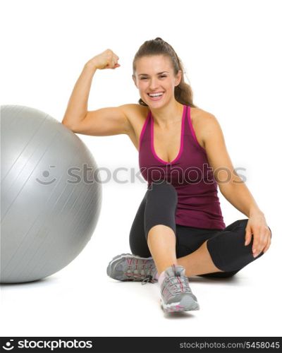 Happy fitness young woman sitting near fitness ball and showing biceps