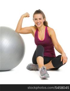 Happy fitness young woman sitting near fitness ball and showing biceps