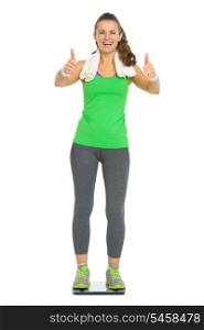 Happy fitness young woman standing on scales and showing thumbs up
