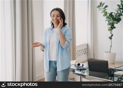 Happy freelancer at workstation. Young european woman is specialist, having phone call. Business woman is working at home office. Remote work and communication online on quarantine.. Happy freelancer european woman having phone call. Remote work and communication online.