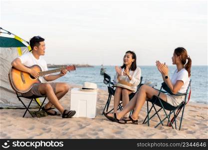 Happy friend have fun playing guitar and clap in camp they smiling together in holiday on sand beach near camping tent vacation time at sunset, Young Asian group woman and man in summer travel outdoor