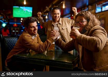 Happy friends having fun arm wrestling during rest at sport bar. Funny guy drinking beer and winning. Happy friends having fun arm wrestling at sport bar