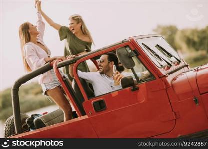 Happy friends having fun in convertible car at vacation by river