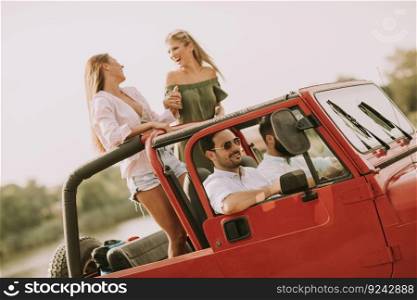 Happy friends having fun in convertible car at vacation by river
