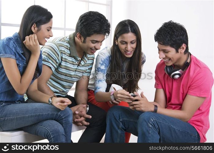 Happy friends looking at mobile phone in college
