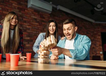 Happy friends plays at the table in cafe. Board game with wooden blocks requiring high concentration, entertainment for funny company. Happy friends plays table game at the table in cafe